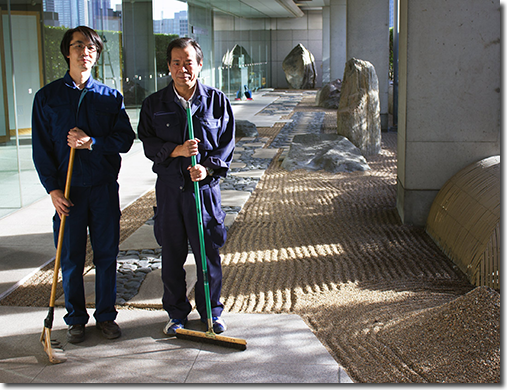 Professional Gardener Mitsuru Machida (left) and co-worker Toshiyuki Uchida, after raking the karesansui portion of the landscape garden at the Canadian Embassy, Tokyo. The long pivoting broomhead with short even bristles is a perfect fit for the grooves made by the wooden rake, providing the raker with more flexibility to reach and to correct channels that can’t be touched using the wooden rake.